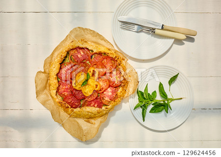 Freshly baked tomato galette on parchment paper served on a rustic wooden table in a cozy kitchen setting 129624456