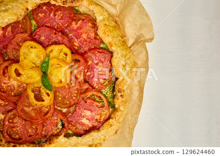 Freshly baked tomato galette on parchment paper served on a rustic wooden table in a cozy kitchen setting Freshly baked tomato galette on parchment paper served on a rustic wooden table in a cozy kitchen setting 129624460