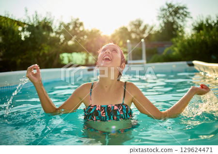 Teen girl enjoying a summer day in a pool, celebrating with arms raised under the warm sun Teen girl enjoying a summer day in a pool, celebrating with arms raised under the warm sun 129624471