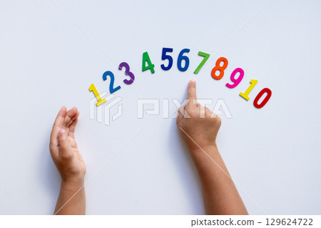 Child hands pointing at colorful wooden numbers on white background Child hands pointing at colorful wooden numbers on white background 129624722