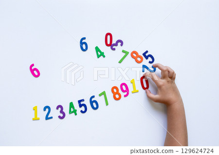 Child hand arranging colorful magnetic numbers on white background 129624724