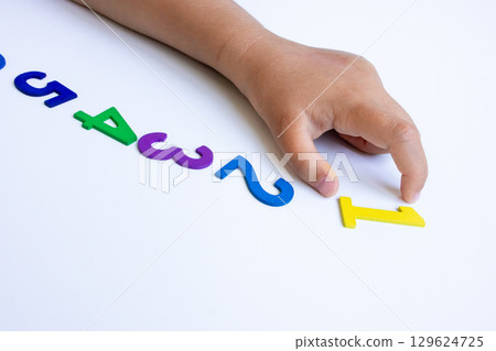 Child hand arranging colorful numbers in sequence on white background 129624725