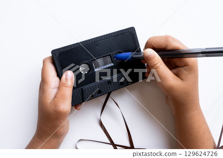 Hands rewinding black cassette tape with pen on white background Hands rewinding black cassette tape with pen on white background 129624726