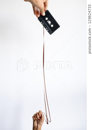Retro vibes. Hand unspooling cassette tape against minimalist white background 129624735