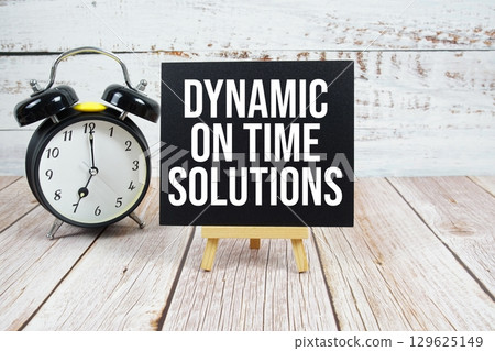 Dynamic On Time Solutions text with easel and alarm clock on wooden background 129625149