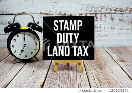 Stamp Duty Land Tax text with easel and alarm clock on wooden background 129625151
