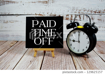Paid Time Off text with easel and alarm clock on wooden background Paid Time Off text with easel and alarm clock on wooden background 129625157