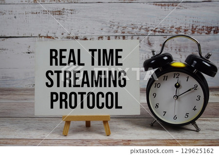 Real Time Streaming Protocol text with easel and alarm clock on wooden background Real Time Streaming Protocol text with easel and alarm clock on wooden background 129625162