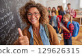 Smiling teacher gesturing thumbs up in classroom with students entering 129626315