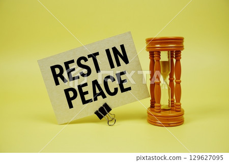 Rest In Peace text message on paper card with hourglass on yellow background 129627095