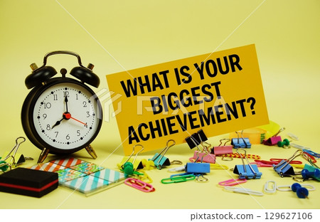 What is Your Biggest Achievement? text on paper card with alarm clock and stationery on yellow background What is Your Biggest Achievement? text on paper card with alarm clock and stationery on yellow background 129627106