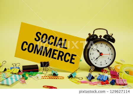 Social Commerce text on paper card with stationery and alarm clock on yellow background 129627114