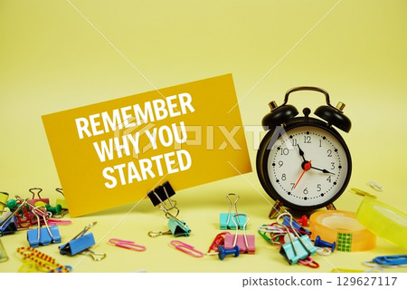 Remember Why You Started text on paper card with stationery and alarm clock on yellow background 129627117