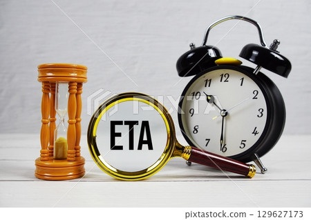 ETA abbreviation of Estimated Time Of Arrival text with alarm clock on wooden background 129627173