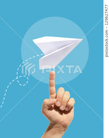 Collage of white paper plane balanced on fingertip with dotted flight path on blue background 129627477