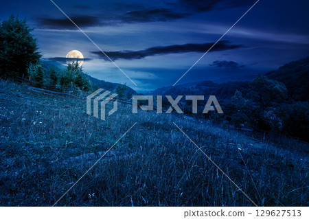 countryside landscape with overcast sky in summer at night. forest on the grassy hill. cloudy weather forecast in full moon light. remote rural scenery in mountains 129627513