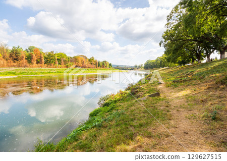 uzh river in autumn. sunny weather. green environment with grassy riverside. trees on the shore and clouds on the sky reflecting in the calm water. urban landscape. global warming background 129627515
