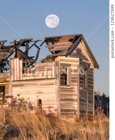 Dilapidated Wooden House Under Moon in Rural Landscape Under Blue Sky 129627999