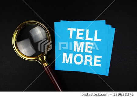 Tell Me More text on sticky note with magnifying glass on black background 129628372