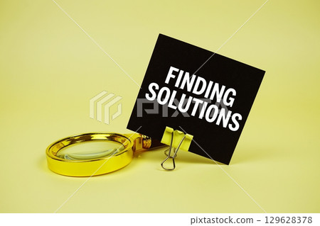 Finding solutions text message on sticky note with magnifying glass on yellow background 129628378