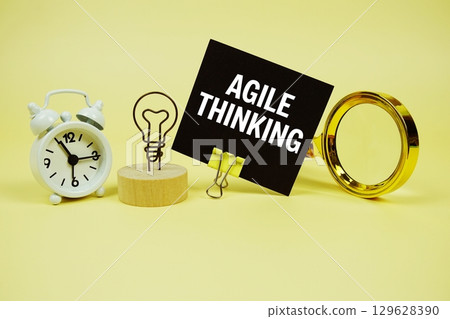 Agile Thinking text message on sticky note with magnifying glass and alarm clock on yellow background Agile Thinking text message on sticky note with magnifying glass and alarm clock on yellow background 129628390