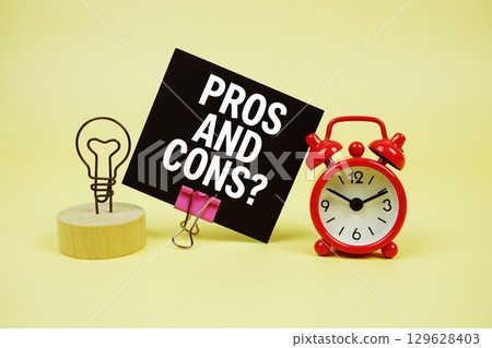 Pros and Cons? text message on paper card with alarm clock on yellow background Pros and Cons? text message on paper card with alarm clock on yellow background 129628403