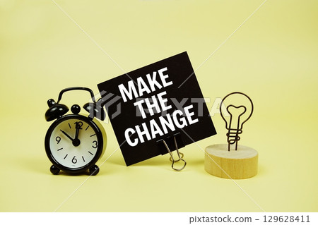Make The Change text message on paper card with alarm clock on yellow background Make The Change text message on paper card with alarm clock on yellow background 129628411
