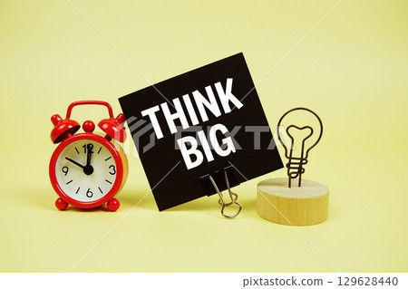Think Big text message on paper card with alarm clock on yellow background Think Big text message on paper card with alarm clock on yellow background 129628440