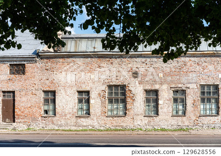 An old, abandoned brick building with weathered walls and broken windows, viewed from across the street 129628556