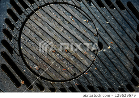 A black grill grate with a hole in the middle. The grate is dirty and has some food particles on it. 129629679