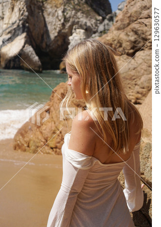 A Serene Beach Model Posed Gracefully by the Rocks in a Beautiful Sunlit Landscape 129630577