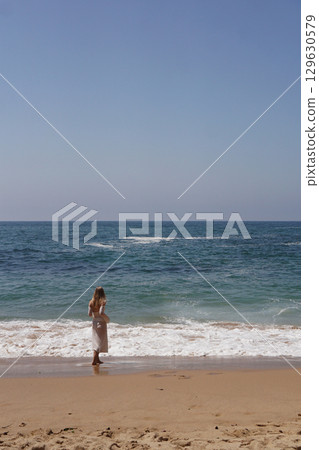 A Serene and Beautiful Beach Scene Featuring a Woman Embracing the Ocean Waves Joyfully 129630579