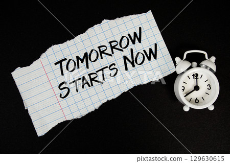 Tomorrow Starts Now text written on paper with alarm clock on black background 129630615