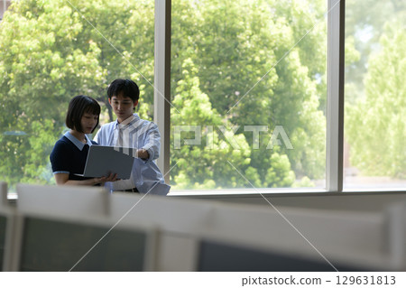 Male and female university students having a conversation by the window with a laptop 129631813