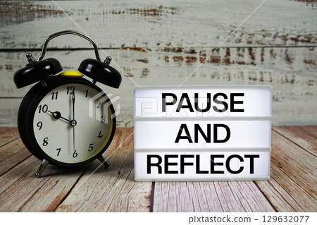 Pause and Reflect text on light box with alarm clock on wooden background 129632077