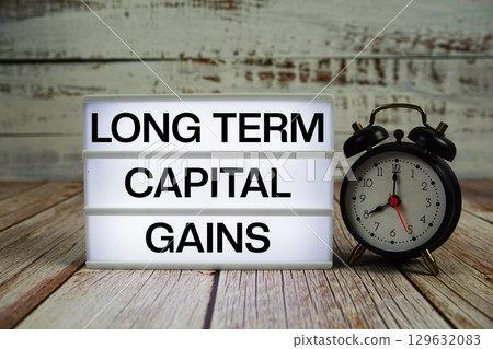 Long Term Capital Gains text on light box with alarm clock on wooden background 129632083