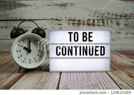 To be Continued text on light box with alarm clock on wooden background 129632089