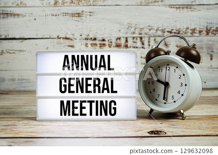 Annual General Meeting text on light box with alarm clock on wooden background 129632098