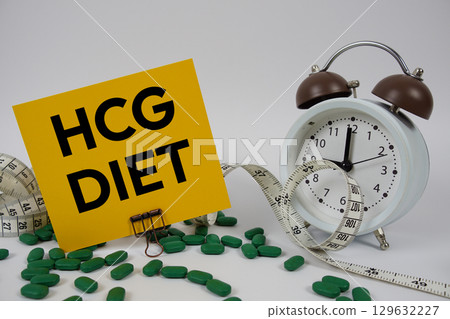 HCG Diet text with medicine, alarm clock and measuring tape on white background 129632227