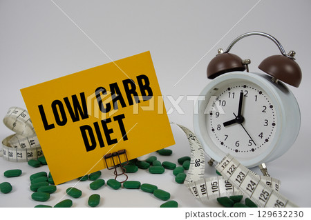 Low Carb Diet text with medicine, alarm clock and measuring tape on white background 129632230