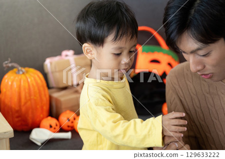Young child exploring Halloween decorations with father 129633222
