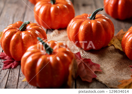 Mini decorative pumpkins on rustic wooden background with autumn leaves 129634014