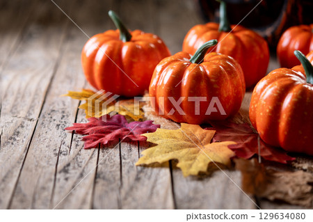 Mini decorative pumpkins on rustic wooden background with autumn leaves 129634080