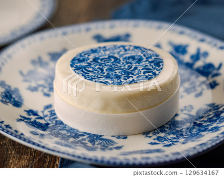 Pastry dessert in Gzhel rustic style. Sweet pastry decorated blue flowers photo printing on sugar paper. Mini cake Gzhel on plate over wooden tabletop background. Closeup 129634167