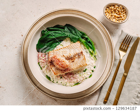 White fish on pillow of pine nut garnished with blanched spinach and white caviar, on restaurant table. Delicious dish with whitefish, top view White fish on pillow of pine nut garnished with blanched spinach and white caviar, on restaurant table. Delicious dish with whitefish, top view 129634187