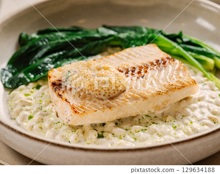 Muksun (Coregonus muksun). Muksun flesh delicacy tender. White salmon fish on pillow of pine nut garnished with blanched spinach and white caviar, on restaurant table. Delicious dish with white fish Muksun (Coregonus muksun). Muksun flesh delicacy tender. White salmon fish on pillow of pine nut garnished with blanched spinach and white caviar, on restaurant table. Delicious dish with white fish 129634188