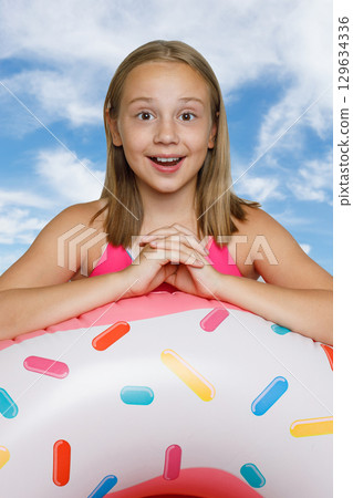 Happy little girl and colorful inflatable ring swimming float against blue sky Happy little girl and colorful inflatable ring swimming float against blue sky 129634336