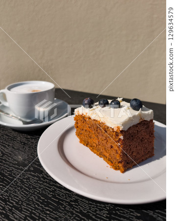 Carrot cake with cream cheese frosting and blueberries served with cappuccino on a table 129634579