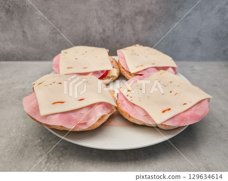 Four tasty sandwiches with ham and cheese lying on white plate copy space 129634614