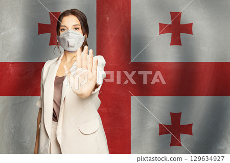 Confident woman in medical mask showing stop gesture open palm hand against flag of Georgia  129634927